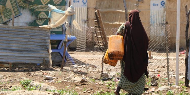 A displaced woman carries water jerry cans at a camp in Guriel town, Somalia. Photo credit: Abdukadir Abdirahman Mohamed/NRC
